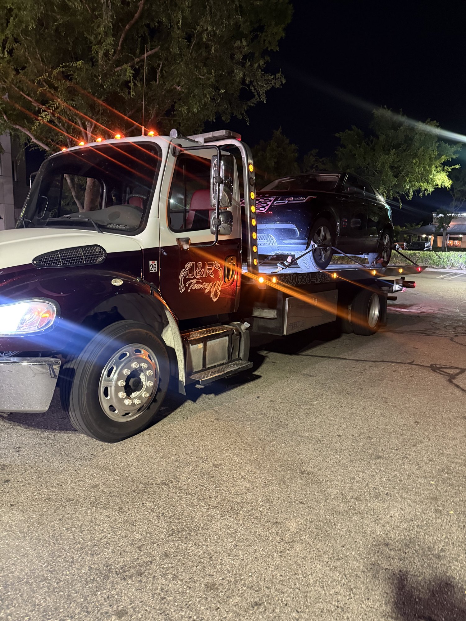 J&R Towing flatbed transporting an SUV at night
